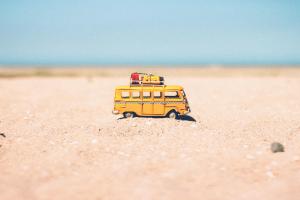 Gelber Spielzeugbully mit Urlaubsgepäck im Sand mit Meer im Hintergrund