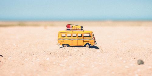 Gelber Spielzeugbully mit Urlaubsgepäck im Sand mit Meer im Hintergrund