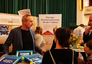 Schulleiter berät Eltern an einem Messestand.