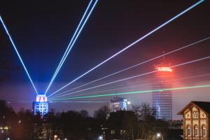 Blick auf das Hochaus von Jenpotik, das bunte Laserstrahlen in den Nachthimmel sendet