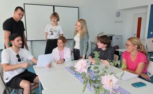 Sieben Erwachsene sitzen in einem Klassenraum um Tische herum