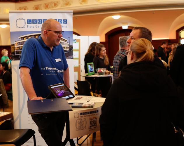 Schulleiter an einem Messestand mit Interessierten.