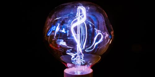 Leuchtende Glühbirne mit sichtbarem Filament vor schwarzem Hintergrund.