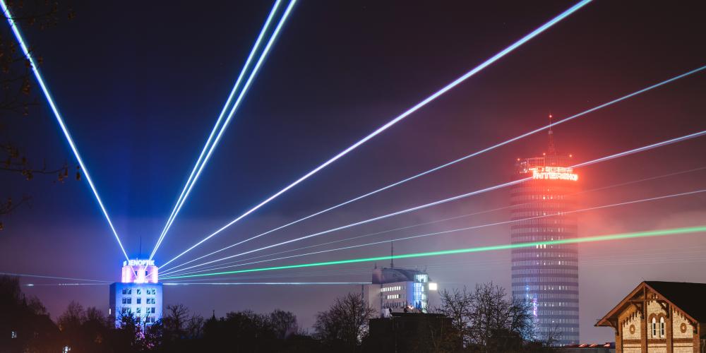 Blick auf das Hochaus von Jenpotik, das bunte Laserstrahlen in den Nachthimmel sendet