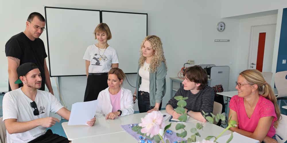 Sieben Erwachsene sitzen in einem Klassenraum um Tische herum