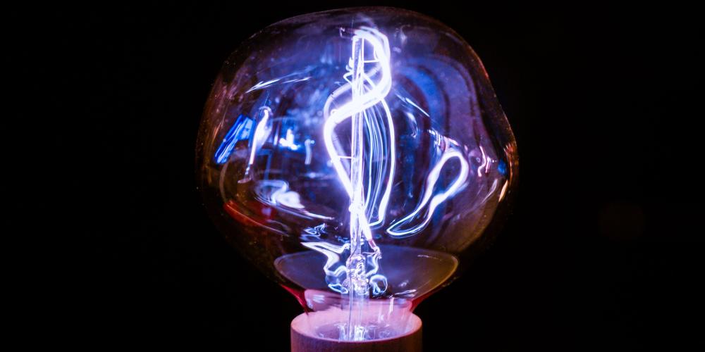 Leuchtende Glühbirne mit sichtbarem Filament vor schwarzem Hintergrund.