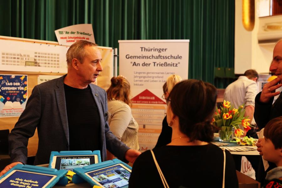 Schulleiter berät Eltern an einem Messestand.