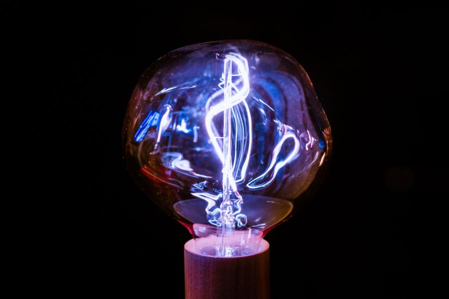 Leuchtende Glühbirne mit sichtbarem Filament vor schwarzem Hintergrund.